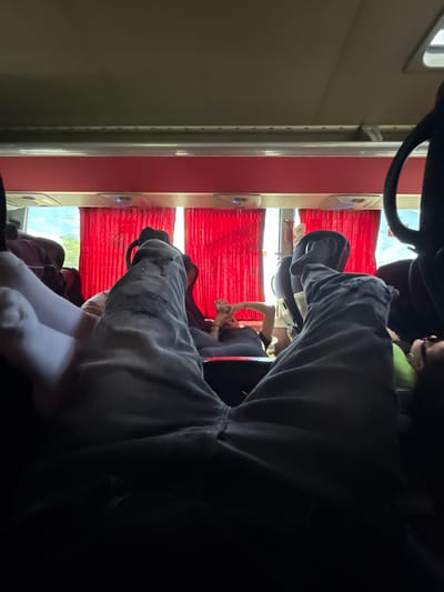 The image appears to be taken inside a train compartment. Red window shades are visible in the background. Several people can be seen sitting in the compartment. The viewpoint is obscured by what seems to be someone wearing a gray hoodie. The location is presumably near Izvorovo, Bulgaria, given the prompt.