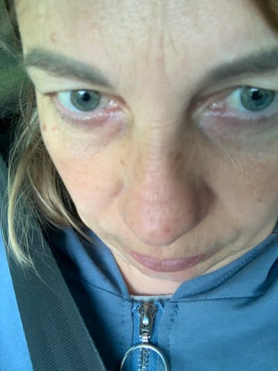 A close-up, high-angle shot shows a person's face, predominantly the eyes, nose, and mouth, from the nose up. The individual has fair skin with freckles and light brown hair. They are wearing a blue zippered jacket. The lighting suggests an outdoor or well-lit indoor environment. The provided location, Мядзельскі сельскі Савет, Belarus, is a rural administrative unit, implying the photo was taken in a village or rural area within that region. The scene captures a moment of personal photography, possibly a selfie, with no other individuals or specific environmental details of the location visible.