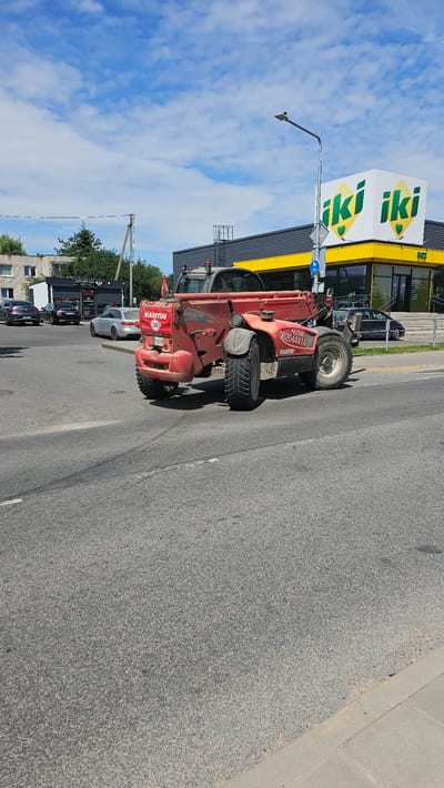 A red Manitou telehandler is parked on a paved road in front of a yellow-trimmed IKI supermarket in Nemėžis, Lithuania. The telehandler has the number "30" in a red circle on its side, indicating a speed limit. The supermarket has large windows and a prominent "iki iki" logo. Several cars are visible in the background. The sky is blue with scattered clouds.
