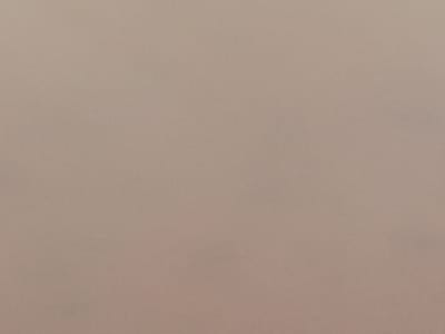 This is a photograph of a textured surface, likely fabric or paper, in a neutral, light brown or taupe color. The texture appears to be fine and slightly grainy, with subtle variations in shading that suggest an uneven surface at a microscopic level. There are no discernible objects, people, or environmental features present in the image. The photograph is a flat, evenly lit shot with no shadows. The location in Nanka, Nigeria, is not visible in this image.