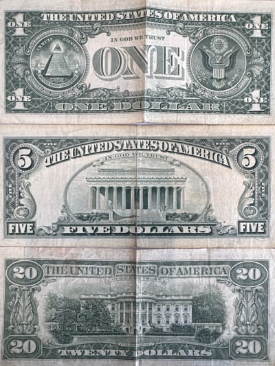 The image displays the reverse sides of three United States dollar bills: a one-dollar bill at the top, a five-dollar bill in the middle, and a twenty-dollar bill at the bottom. The one-dollar bill features the Great Seal of the United States on the left and an eagle on the right. The five-dollar bill shows the Lincoln Memorial in the center. The twenty-dollar bill depicts the White House. The bills are laid out vertically and slightly overlapped. There is no indication of the city of Mejaniga, Italy, or any other specific geographical location. The image is a close-up shot of these currency denominations.