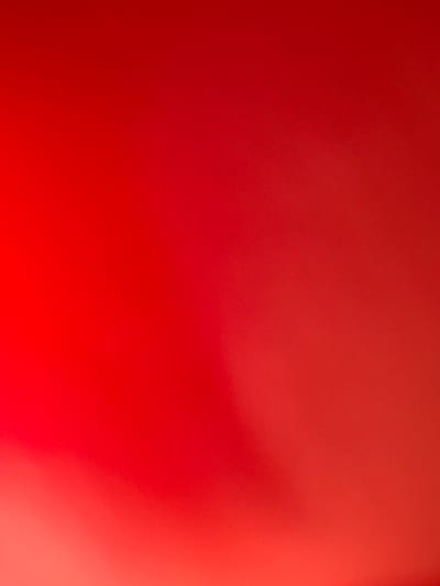 The image presents an abstract composition dominated by varying shades of red, transitioning across the frame. The top and left portions feature a darker, deeper red, gradually shifting to a brighter, more vibrant, and slightly orangey-red towards the bottom and right sides. This creates a smooth, out-of-focus gradient effect. The entire image is soft and blurred, lacking sharp details or discernible objects. There is a very subtle, fine-grained texture visible across the surface, but it does not form any recognizable patterns or shapes.

No specific subjects such as people or distinct objects are visible. The scene is purely abstract, focusing on color and light. There is no activity or event taking place. The image does not provide any cues regarding the time of day, weather conditions, or specific location within Gravesham, United Kingdom, or anywhere else. There is no visible text. The overall impression is one of warmth, intensity, and minimalist design, emphasizing the interplay of red hues and soft light.