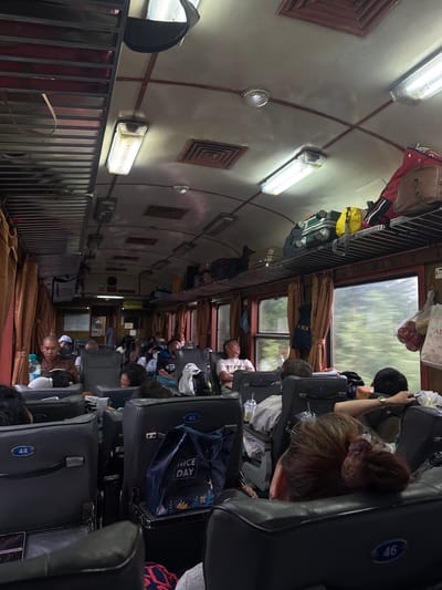 The image depicts the interior of a passenger train car, possibly in Ninh Đông, Vietnam, filled with seated passengers. The lighting is dim, with fluorescent tubes illuminating the ceiling. Luggage is stored on overhead racks. Several passengers appear to be resting or sleeping, with some leaning against the seats or windows. The seats are upholstered in dark material and arranged in rows facing each other. Curtains are drawn across the windows. The overall atmosphere suggests a long journey.