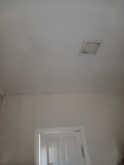 The image shows an indoor ceiling and upper wall area. A white square fixture, possibly a light or vent, is visible on the white ceiling. The ceiling shows some faint discoloration or water stains. The upper part of a white interior door is visible at the bottom center of the image, with a white doorframe. The walls are painted a light, neutral color. The scene appears to be a residential interior. No people or specific actions are depicted. The location in Vashkivtsi, Ukraine is not visually apparent from the image itself.
