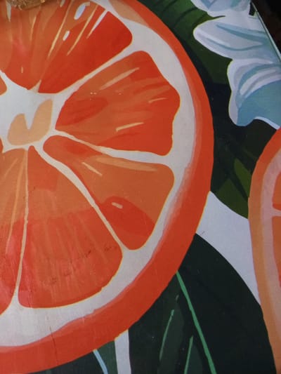 Close-up of a decorative surface depicting sliced oranges, green leaves, and a light blue flower. No people are visible. Location information is not present in the image.