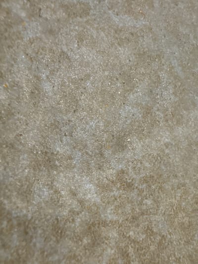 The image is a close-up, textured, abstract view of a sandy or granular surface. The color palette is dominated by light browns, beiges, and whites, with numerous small, reflective particles scattered throughout, suggesting the presence of mica or other crystalline materials. There are no discernible objects, people, actions, or interactions visible. The image provides no information about its location in the city of Astrashitskagaradokski rural council, Belarus, or any environmental context beyond the surface itself.