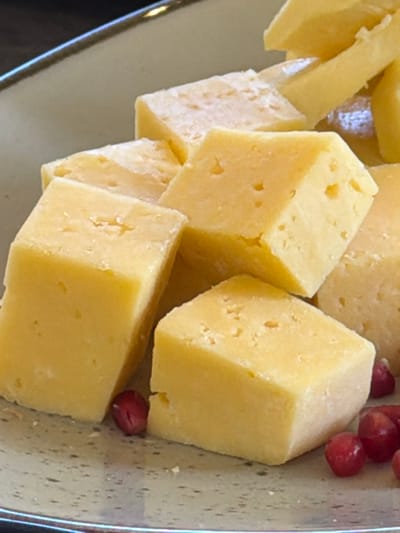 The image shows a plate or container filled with yellow, cube-shaped pieces of cheese. Several smaller, triangular pieces of cheese are also present. A few small, red berries are nestled among the cheese cubes. The background appears to be a speckled surface, possibly the interior of a serving container.

It is not possible to determine the location of this image as Lermontovo, Armenia, or any other specific city from the image alone.