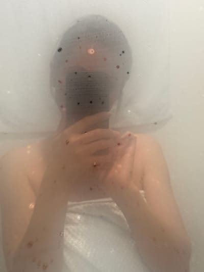 The image shows a person submerged in a bathtub filled with cloudy water. The person is wearing a dark cap or head covering. Their arms are crossed over their chest. The background appears to be the white interior of the bathtub. There is no visible indication of the location being Kranj, Slovenia.