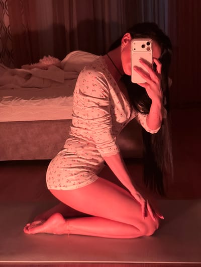 A woman is lying on a bed taking a selfie with her phone. She is wearing a floral patterned pajama set. Her long dark hair is spread out. The location cannot be determined from the image, and is not Svkh Voronezhskiy, Russia.