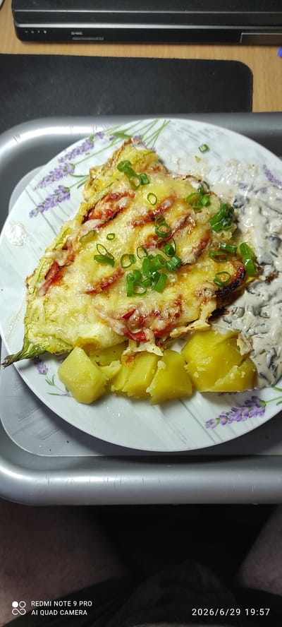 A close-up, top-down shot displays a slice of baked zucchini with melted cheese and chopped green onions, served on a white plate with a lavender pattern. To the right of the zucchini slice, a portion of creamy sauce with visible mushroom pieces is present. In the bottom left of the plate, several diced boiled potatoes are arranged. The plate rests on a grey, textured tray. The background shows a black surface, possibly a desk or laptop, with a black object in the upper portion of the frame. A watermark in the lower left corner reads "REDMI NOTE 9 PRO AI QUAD CAMERA", and the date "2026/6/29 19:57" is visible in the lower right. There is no indication of the city of Maardu, Estonia in this image.