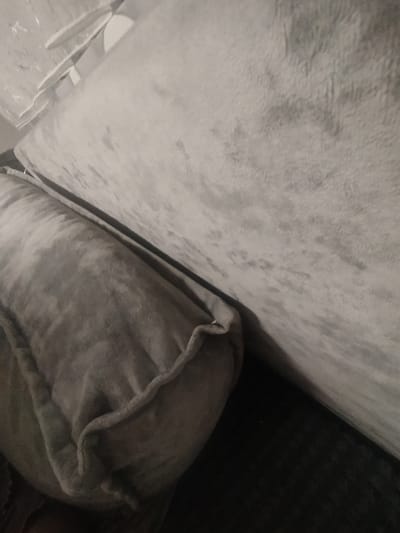 The image shows a close-up, angled view of a grey, plush sofa. The sofa appears to be made of a soft, velvety fabric, with a slight sheen that catches the light. In the foreground, a bolster pillow, also grey and plush, is positioned horizontally. Its edges are neatly piped and slightly rounded. Behind the bolster, the main body of the sofa stretches diagonally across the frame, revealing its textured surface.
The lighting is dim and appears to be artificial, casting soft shadows and highlighting the textures of the fabric. The overall color palette is monochromatic, dominated by shades of grey. There is no visible text or any indication of people or specific activities. The image focuses solely on the textural details of the sofa and pillow, suggesting an indoor setting, likely a living room. The composition is abstract, emphasizing form and texture over narrative or context. The scene is static and peaceful, conveying a sense of comfort and softness associated with the furniture. No specific time of day or weather conditions are discernible.