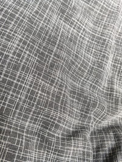 The image shows a close-up view of a grey fabric with a white, crisscrossing line pattern. The fabric appears to be textured and slightly wrinkled, indicating it might be a woven material such as linen or cotton. The lines are uneven and some are thicker than others, creating a somewhat abstract, grid-like effect. The lighting highlights the texture and the folds of the fabric. There is no indication of a city, camp, or any specific location in Russia in this image.
