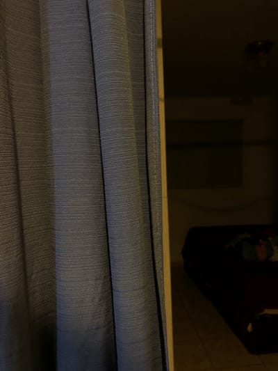 The image shows a close-up view of stacked, folded fabric, likely curtains or similar material. The fabric has a ribbed texture, appearing in shades of blue and grey. Above the fabric, a portion of the room is visible, including a door and a dark object which might be furniture. The location is not discernible from the image. There is no indication of the city of Rio Grande, Argentina. There are no people in the image.