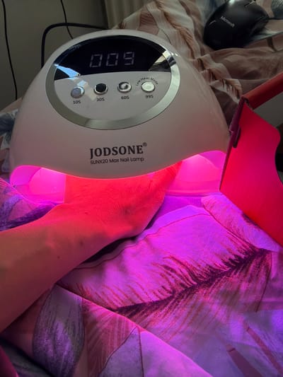 The image shows a hand inside a JODSONE SUNX20 Max Nail Lamp. The lamp is turned on and displaying "009" on its digital timer. The buttons for "Low Heat Mode," "10S," "30S," "60S," and "99S" are visible on the lamp. Next to the lamp is a Microsoft computer mouse. The background includes a patterned surface that looks like a blanket or bedding. There is no verifiable evidence in the image to associate the scene with the city of Bearpark, United Kingdom.