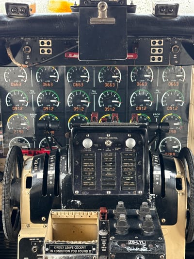 The image shows the interior of an aircraft cockpit, specifically the control panel. The panel features a series of gauges including engine RPM (NG), propeller RPM (PROP), and fuel flow (FF). Various controls are visible, including a throttle quadrant with settings for FLIGHT, IDLE, GND IDLE, and MAX REV. There's a switch panel with labels such as PRIMARY FUEL PUMP FAILURE, LOW ENG. FUEL BOOST PRESS, OIL PRESS LOW, and AUTO FEATHER ARMED, among others. An RPM SYNC CONTROL is also present. A label reads "KINDLY LEAVE COCKPIT IN CONDITION YOU FOUND IT," and a plate displays the registration "ZS-LYL."

The location in Kraaifontein, South Africa, cannot be determined from the image alone.