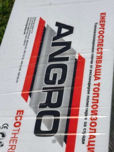 The image shows a close-up of a package of "ANGRO ECOTHERI" thermal insulation boards made of expanded polystyrene. The packaging includes Bulgarian text stating the product is "energy-saving thermal insulation." The manufacturer's contact information is provided as located at 114 Europa Blvd, Sofia, Bulgaria. The city of Selyanin is not directly mentioned on the product packaging or immediately discernible from the image itself.