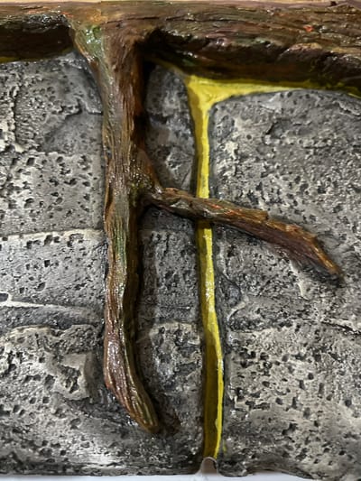 The image is a close-up, overhead shot of a textured, grey, brick-like surface with a brown, branch-like object extending from the top and a thick, yellow, fluid-like substance dripping down the grey surface. The branch is glossy and appears to be wet, with visible texture and some green and reddish hues. The yellow substance is also glossy and appears to be actively flowing downwards, creating a viscous effect. The grey surface has a rough, porous texture that resembles weathered stone or concrete. There are no people or clear indicators of location within the city of Kalininskaya, Russia. The image focuses solely on the abstract texture and composition of the objects.