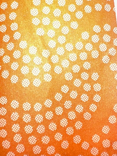 The image is a close-up, top-down view of an orange surface with a repeating pattern of small white circular shapes. Each white circle contains a grid of smaller dots. The orange surface has a slightly textured, gradient appearance, transitioning from a brighter yellow-orange in the upper left to a deeper orange towards the bottom right. This image does not contain any information that would allow for the identification of a specific location in Letterkenny, Ireland, nor does it depict any people, actions, or interactions.