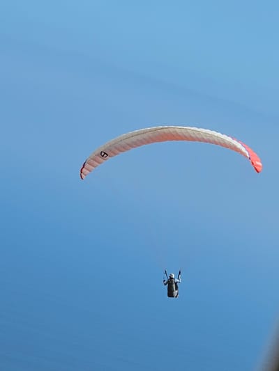 A paraglider with a red and white wing is flying in a clear blue sky. A person wearing a jumpsuit and a helmet is harnessed to the paraglider and appears to be in flight. The location is inferred to be near Alto Hospicio, Chile, based on the image request.