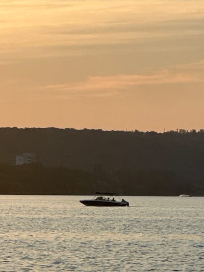 In the city of Ustia, Moldova, at dusk, a boat with several passengers is visible on the water, with a dark hill in the background. The sky is a soft orange with wispy clouds.