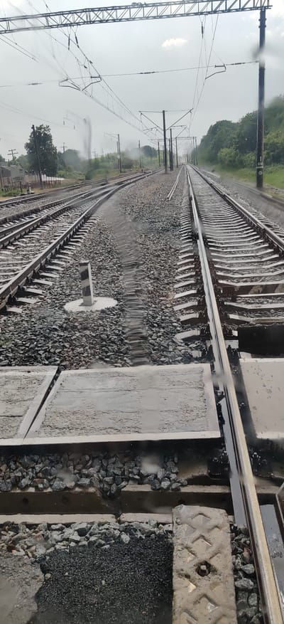 The image depicts a view of multiple train tracks, likely in a rural or suburban setting, given the presence of trees and a cloudy sky. The tracks appear to be part of a railway yard or junction, as evidenced by the converging and diverging lines of rails. Some of the tracks are covered in gravel ballast, while others have concrete sleepers. There are overhead electrical wires and poles visible, indicating an electrified railway line. The ground around the tracks is wet, suggesting it has recently rained or is currently raining, and there are puddles of water visible. A small, striped marker post is present near the center of the image. The overall scene is one of infrastructure for transportation in potentially inclement weather.
The specific location in the city of Shelestove, Ukraine, is not directly discernible from the visual information presented in the image. While the image shows railway tracks and associated infrastructure, there are no unique landmarks, signage, or contextual clues that would definitively place it in Shelestove or any other specific city. Therefore, any statement about the location being Shelestove, Ukraine, would be an assumption or external information not derivable from the photograph itself.