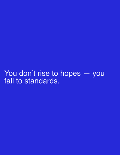 The image is a text-based image with a solid blue background. The text, written in white, reads: "You don't rise to hopes - you fall to standards."
There is no indication of a location in Woking, United Kingdom or any other identifiable location. There are no people, objects, actions, interactions, or environmental elements beyond the text and background color.