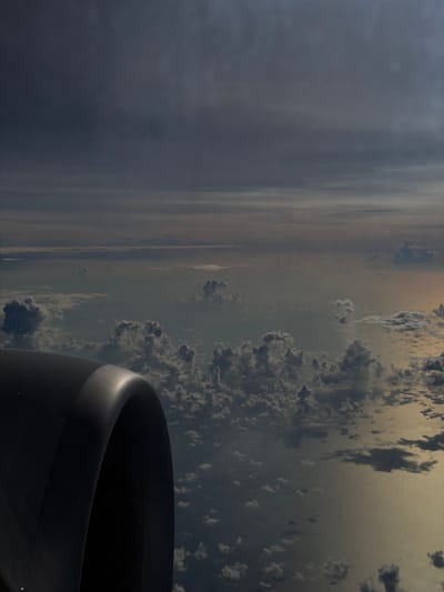 An image taken from an airplane window shows the wing and engine of the aircraft. Outside the window, there is a view of clouds and landscape below. This image does not appear to be taken in the city of Taoyuan City, Taiwan.