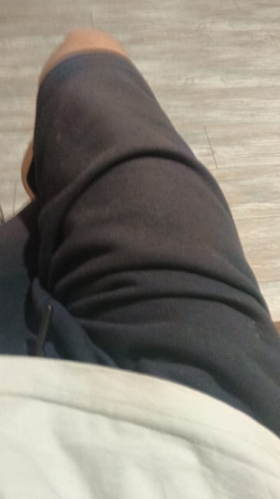 The image shows a close-up view of a person's legs, with one leg covered by dark pants and the other partially visible, appearing bare. The background consists of a light-colored wooden floor. There is no information in the image to suggest it is located in Aksinyino, Russia.