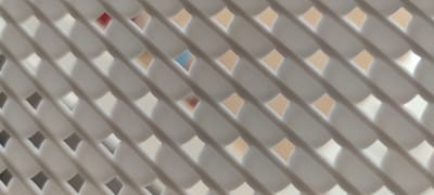 This media file displays a close-up, abstract view of a white, textured surface with a repeating pattern of diagonal lines and circular or diamond-shaped openings. The texture appears to be slightly raised or embossed, creating a visual effect of depth. Through the openings, glimpses of a background can be seen, suggesting a layered or semi-transparent structure. Some of these background elements are out of focus, showing subtle shifts in color, including hints of beige, white, and what appears to be a touch of pink or red in one small area, and a pale blue in another.
The lighting is soft and diffused, creating gentle shadows that enhance the texture and form of the white surface. There is no discernible activity or event taking place, as the focus is entirely on the abstract pattern and texture of the object. No people, specific objects, or clear environmental cues are visible that would indicate a particular time of day, weather, or emotions. The image has a minimalist and somewhat geometric aesthetic. There is no visible text within the frame. The context provided is Liebenburg, Germany, but this information is not visually derivable from the image itself.