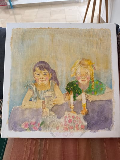 This is a painting on canvas of two young girls sitting at a table. The girl on the left has dark hair pulled back in a ponytail and is wearing a striped dress. She is holding a glass. The girl on the right has blonde hair in braids and is wearing a green shirt with a floral pattern. Two lit candles and a vase of flowers are on the table between them. The background is a soft blend of blue and yellow. The painting is unframed and the edges of the canvas are visible.