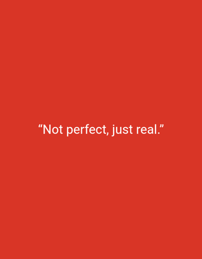 The image shows a solid red background with the quote "Not perfect, just real." centered horizontally and vertically in white text. The words are simple and straightforward, suggesting a theme of authenticity over flawlessness. The red background provides a bold contrast to the text, making the message stand out. The overall impression is one of simplicity and self-acceptance.