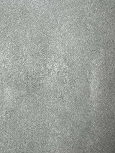 This is a full-frame, high-angle, abstract, close-up shot of a textured, grey surface. The surface has a fine-grained, speckled appearance with subtle variations in tone, suggesting it could be concrete, stone, or a similar material. There are no discernible subjects, objects, or a specific scene depicted. The lighting appears even and diffused, with no strong shadows or highlights, making it difficult to determine the time of day or any specific weather conditions. The overall impression is one of a neutral, unremarkable surface, possibly a wall, floor, or pavement. There is no visible text or any indication of activity, event, or emotional context. The location context provided is Bydlino, Poland, but this information cannot be derived from the image itself.