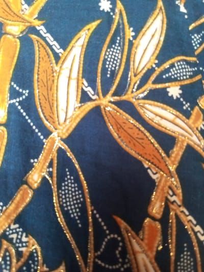 The image shows a dark blue fabric with a golden botanical pattern. The design features bamboo stalks and leaves outlined in gold. The leaves are filled with white or light brown colors and dotted with white patterns. A chain-like border and tiny star-like details are scattered across the background, adding visual interest to the patterned fabric.