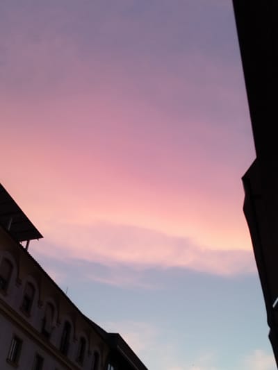 The image depicts a twilight sky with hues of pink and purple transitioning to a pale blue. A portion of a building, likely in the city of Jerez, Spain, is visible in the lower left quadrant. The building has a mansard roof and multiple arched windows. A dark, angular structure, possibly another building or architectural element, occupies the right side of the frame, obscuring part of the sky. The scene is static, with no visible people or ongoing actions. The environment appears to be urban, characterized by the presence of the building against the backdrop of the evening sky.