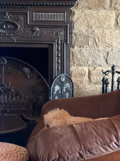 The image shows a stone wall partially obscured by a black, ornate fireplace with a curved grate. A brown cushion or furniture element is present on the right side, partially covering the fireplace. The image lacks context for location confirmation within Кирково, Bulgaria.