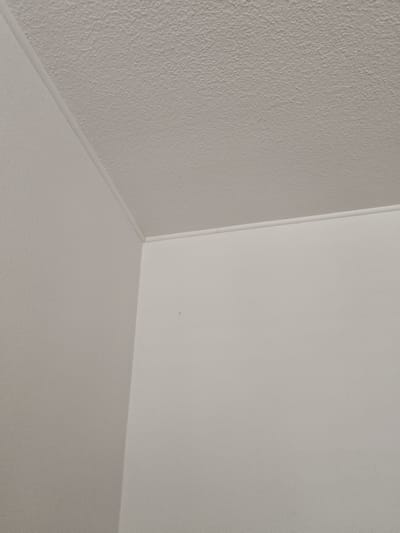 The image shows an interior view of a corner where a textured ceiling meets two plain walls. The walls and ceiling are painted in a neutral, light color, likely white or off-white. A thin, white decorative molding separates the ceiling from the walls. The ceiling has a subtle, bumpy texture, while the walls appear smooth. There is a small, dark speck visible on the wall in the right portion of the image. No people, objects, or actions are depicted. The scene is consistent with the interior of a room, potentially in a residential or commercial building. There is no information within the image to suggest a specific location in Magdeburg, Germany.