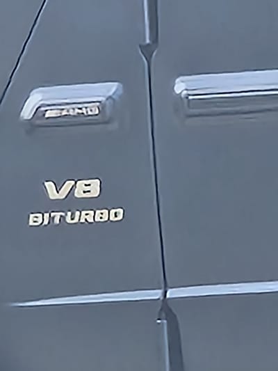 The image shows a close-up of the side of a gray Mercedes-AMG car. The words "AMG" and "V8 BITURBO" are visible on the side. The location is unknown, so I cannot confirm if it is located in Witton Gilbert, United Kingdom.