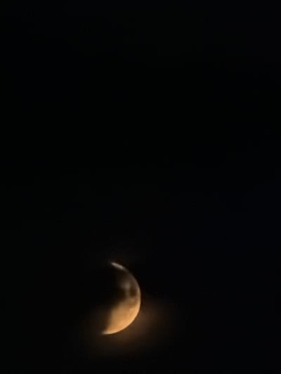 The image shows a crescent moon against a black sky. The moon is illuminated on its right side and appears to be a warm, golden color. The rest of the moon is in shadow. The sky is completely dark, with no other celestial bodies visible. There are no people, objects, or any indication of a city or location in the image. Therefore, it is not possible to determine if the image is from Petukhi, Russia, or any other location.