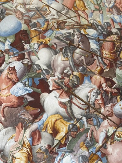 This is a fresco painting depicting a chaotic battle scene with many figures on horseback. The subjects are soldiers in historical armor and clothing, wielding spears, swords, and shields. Several horses are prominently featured, some white, others brown and grey. The composition is dense, with figures overlapping and creating a sense of intense action. The color palette includes muted tones of browns, greys, whites, and reds, with accents of blue and yellow.

The event captured is a fierce cavalry engagement. Soldiers are shown lunging with their weapons, and the horses appear to be in full gallop, adding to the dynamism of the scene. The expressions on the faces of the soldiers are difficult to discern due to the scale and style of the painting, but the overall impression is one of intense conflict and struggle.

Notable details include the ornate armor worn by some of the riders and the various styles of helmets and shields. The fresco appears to be a ceiling or wall painting, given its perspective and the way the figures are arranged. There are no visible cues for time of day or weather. The setting is an interior space, likely a grand hall or chapel, suggested by the fresco style and historical context of San Lorenzo De El Escorial, Spain. No visible text is present in the image.