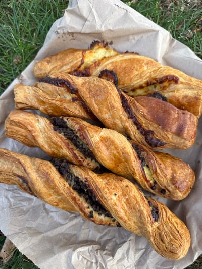 Four twisted pastries rest on brown paper. The background shows green grass, indicating an outdoor setting. The pastries vary in filling, with some appearing to contain cheese and others a dark, possibly chocolate, filling. No people or specific landmarks are visible to confirm the location in High Wycombe.