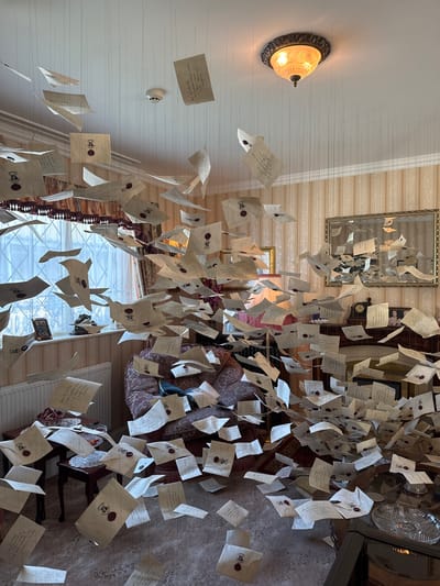 The image shows a room decorated with numerous suspended letters resembling those from the Harry Potter series. The letters are attached to the ceiling by thin strings, creating the illusion of them floating in mid-air. The room appears to be a domestic interior, with furniture visible in the background, including a sofa, a table, and possibly a bookshelf. There is a light fixture on the ceiling and a mirror hanging on the wall. The letters themselves are addressed to Mr. H. Potter and bear the Hogwarts seal. The location and city mentioned, Nerima, Japan, cannot be confirmed with the provided image alone.