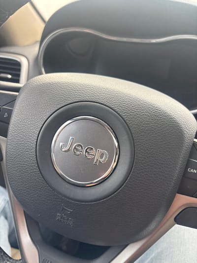 A close-up shot depicts the steering wheel of a Jeep vehicle. The central hub of the steering wheel features a silver "Jeep" logo encased in a black, textured material. The steering wheel also has airbag labeling. The surrounding dashboard elements, including portions of the instrument panel, and vent are visible. The location of this image in Sanctorum, Mexico cannot be determined from the visual data provided.