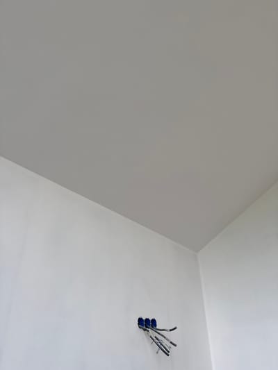 The image captures an interior scene, likely a room under construction or renovation, with a focus on a section of the wall and ceiling. The setting is stark and minimalist, characterized by smooth, unadorned surfaces in varying shades of gray and white.
The primary subjects are electrical wires emerging from an opening in the white wall. These wires are bundled together and appear to be connected to blue electrical boxes. Their exposed state suggests that the electrical installation is in progress, or that the wall is yet to be fully finished. The rest of the visible surfaces are painted walls and ceiling, meeting at a sharp angle, creating a sense of depth and architectural lines.
There are no people visible in the image, nor any explicit indication of the time of day or weather. The lighting appears to be consistent, suggesting indoor lighting or natural light from an unseen source that uniformly illuminates the space. The overall mood is neutral, perhaps even sterile, due to the absence of decorative elements and the clean, unfinished aesthetic.
No text is visible in the image. The location context provided is Zhabkino, Russia, but there are no specific visual cues within the image itself that directly corroborate this location. The scene is generic and could represent a similar construction site anywhere.