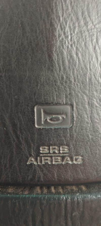 The image shows a close-up of a black leather steering wheel. In the center of the steering wheel, there is a silver emblem with a horn symbol above the words "SRS AIRBAG" embossed in silver. The texture of the leather is visible, with its natural grain and creases. The lighting appears to be even, with no harsh shadows. There are no people or other objects visible in the frame. The image does not provide any information that would allow for the determination of its location in the city of Покосное, Russia.