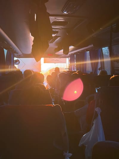 The image shows the interior of a bus with multiple rows of seats, most of which appear to be occupied. Sunlight is streaming through the front of the bus, creating a bright glare that obscures some details. A luggage rack is visible on the left side, and the word "HIGER" appears on a panel near the front. A small globe-like object rests on the floor beneath the luggage rack. The image is strongly lit and slightly disorienting, likely taken from a low angle. There is no visual evidence confirming the location to be Ustinovo, Russia.