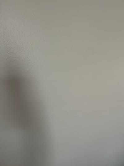 A soft shadow, possibly of a person's head and shoulder, is visible on a light gray painted wall. The wall has a slightly textured, matte finish. The shadow is cast from the left side of the image and tapers off towards the center and right. There are no other discernible objects or people in the frame. The scene appears to be an indoor wall. The location within West Hartford, United States of America, cannot be determined from the visual information provided.