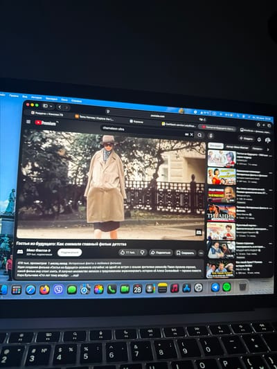 The image shows a close-up view of a laptop screen displaying a YouTube page. The laptop is likely situated in Lørenskog, Norway, as indicated by the presence of "Temu Norway | Explore the L..." in the browser tab. The YouTube video playing is titled "Гостья из будущего: Как снимали главный фильм детства" (Guest from the Future: How the Main Childhood Film Was Filmed). The video thumbnail features a woman in a long coat and hat. Below the video title, the uploader "Микс Фактов" (Mix Facts) is listed with "329 тыс. подписчиков" (329 thousand subscribers). The video has "478 тыс. просмотров" (478 thousand views) and was uploaded "1 месяц назад" (1 month ago). A description of the video mentions interesting facts about beloved films and the creation of the film "Guest from the Future." Several related videos are displayed on the right side of the screen, including titles like "ФАКТЫ О ФИЛЬМЕ" (Facts About the Film), "ТИТАНИК" (Titanic), and "Кто такой Хуан?" (Who is Juan?). The laptop's keyboard and dock are visible at the bottom of the image.