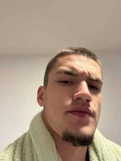 A close-up, low-angle shot of a man's face with a light-green towel visible around his neck. He has short hair and a short beard. The background is a plain white wall. No information about the location in Kisyovtsi, Bulgaria is available.