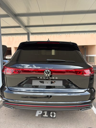 The image shows the rear of a black Volkswagen Touareg parked in what appears to be an indoor or covered parking space. The car is positioned in a parking spot labeled "P1" in white lettering on the asphalt. The vehicle's badging and taillights are clearly visible. The surroundings suggest a parking garage or covered area, with a beige wall and metal structures visible in the background. The location is Ouahat Sidi Brahim, Morocco. No people are visible in the scene.