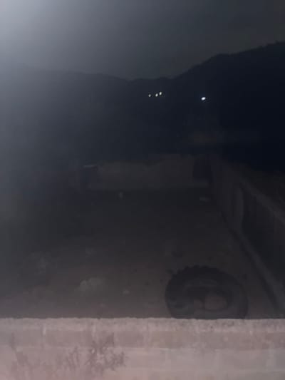 A dark, blurry image depicts what appears to be the underside of a structure. A tire is mounted on a wall or support beam. The support structure has visible texture, suggesting it's made of a rough material like concrete. In the left, there are faint glimmers of light suggesting there may be something beyond the supporting structure. The overall visibility is low.